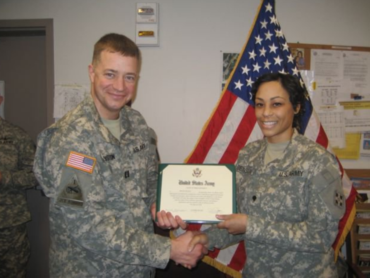 Two soldiers holding a certificate in front of an american flag.